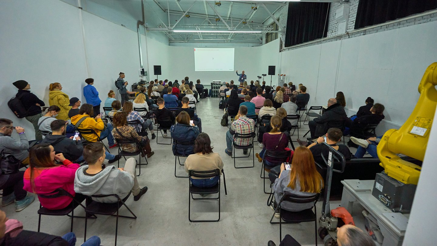 Presenter gesturing toward a diagram during a seminar in a warehouse.