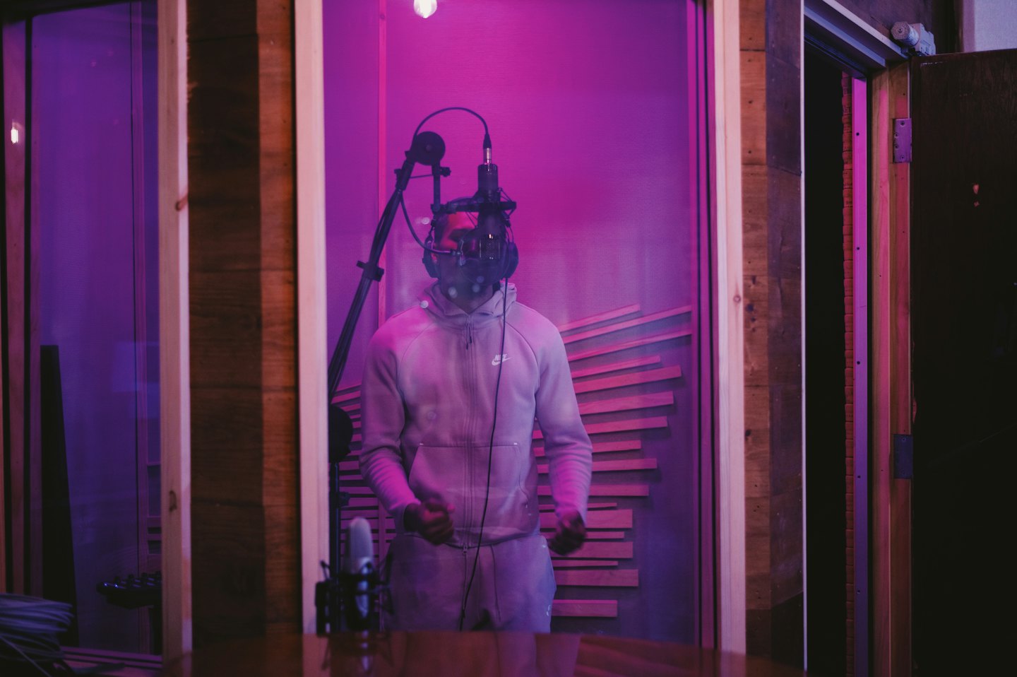 Man singing into microphone in a purple-lit vocal booth.
