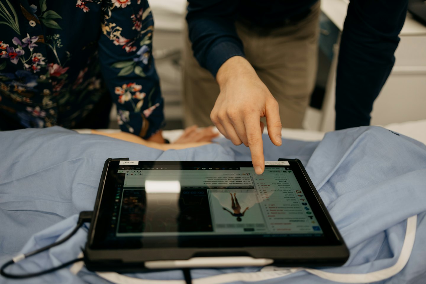 Person's hand points to medical data on a tablet screen.